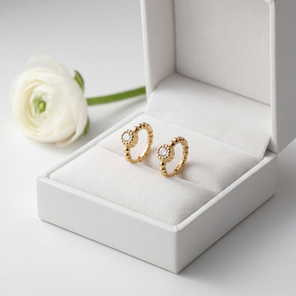 Gold earrings in a white jewelry box with a white flower on a light gray background
